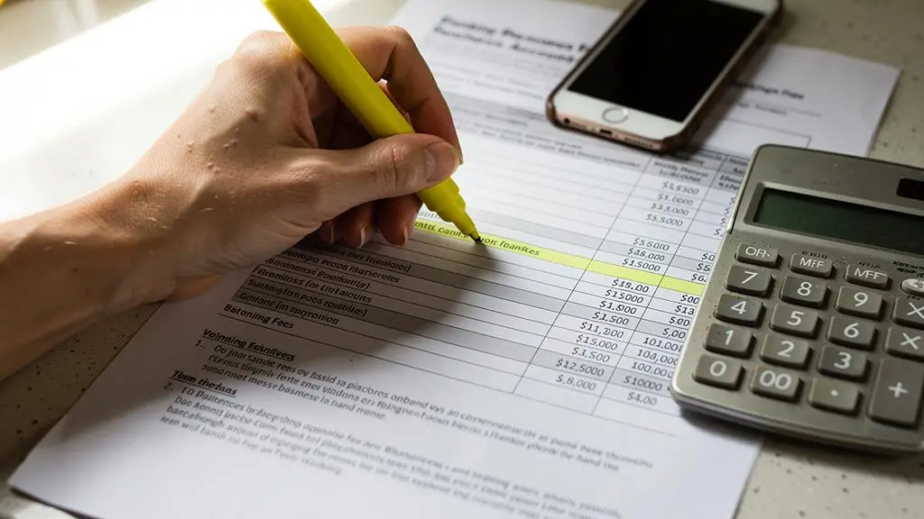 Une main surligne une ligne de frais bancaires sur un document posé près d'une calculatrice.